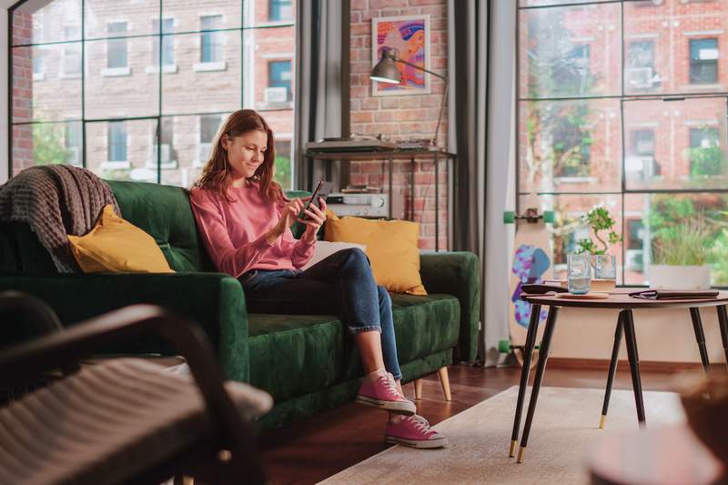 Woman sitting on a sofa in a bright loft apartment checks her phone.