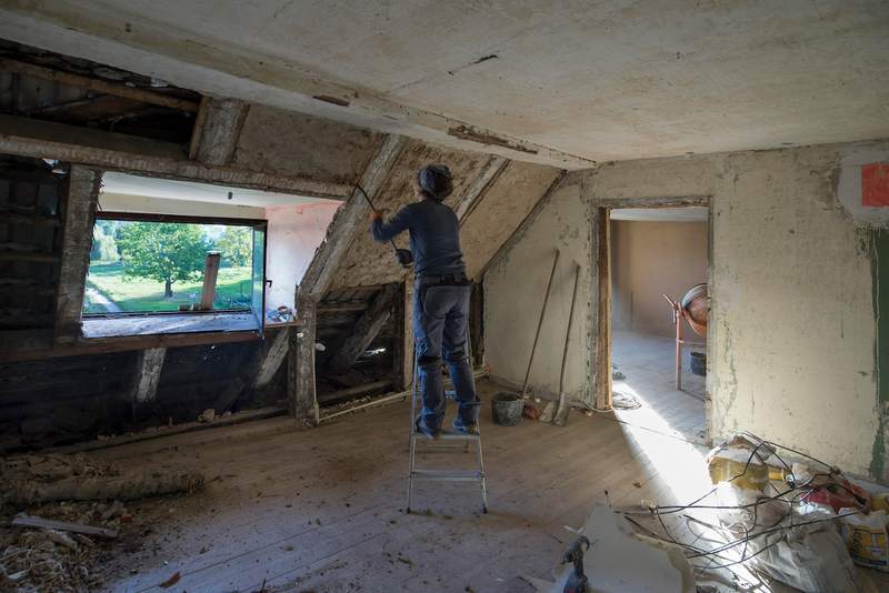 A woman strips the walls in the attic of a fixer-upper home.
